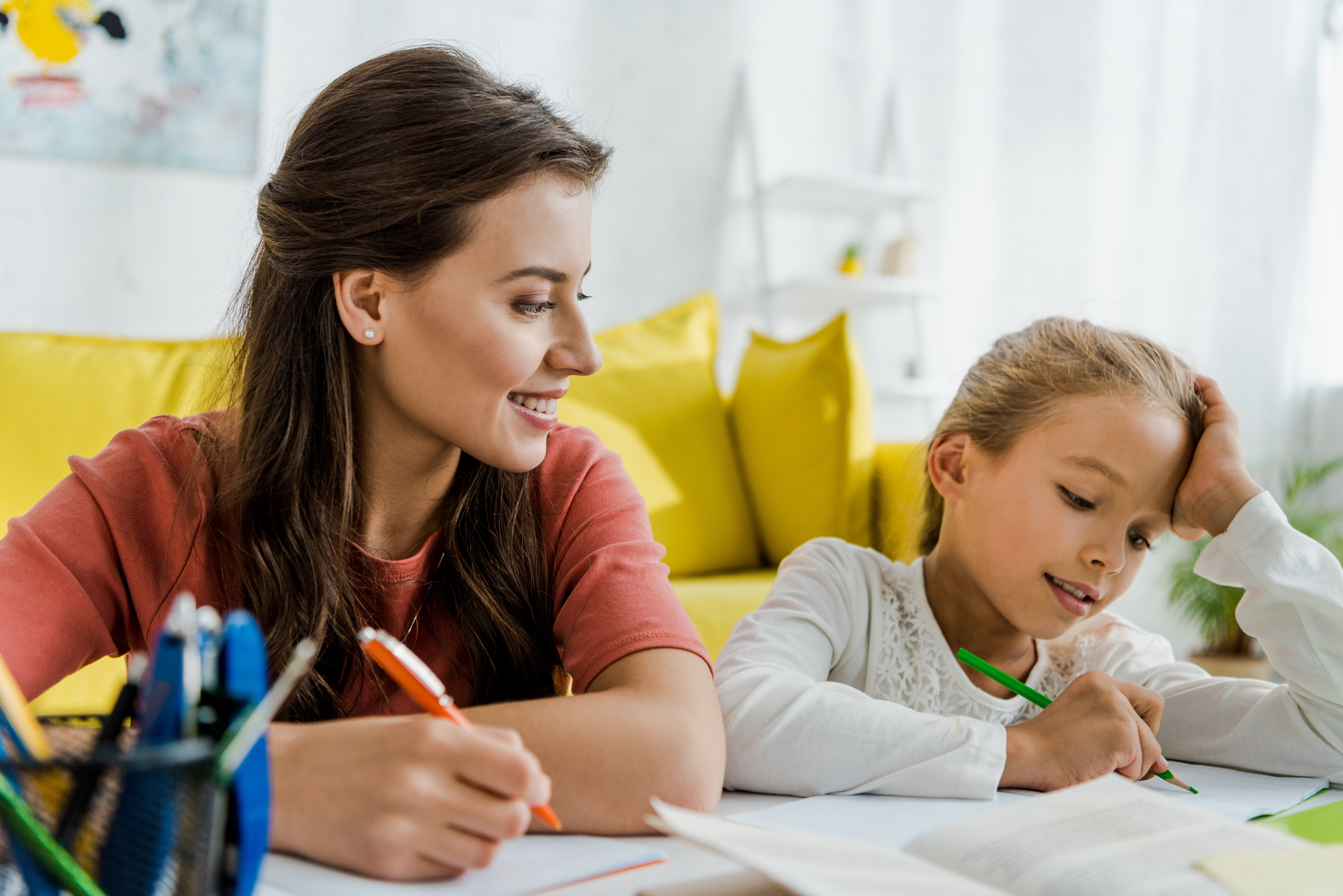 selective focus of happy babysitter looking at kid studying in living room